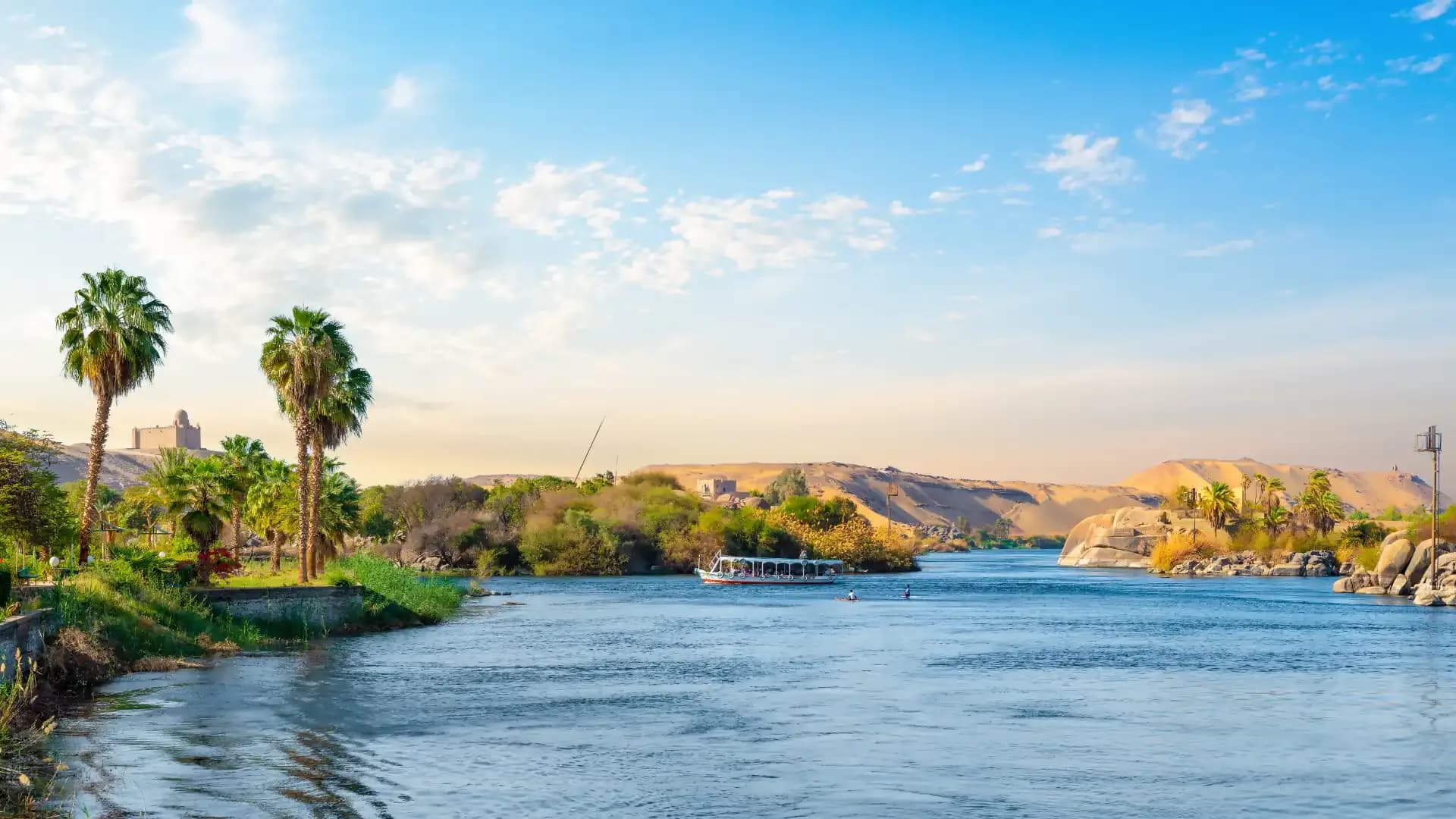 The Nile at Aswan with palm trees, dunes and the Aga Khan Mausoleum