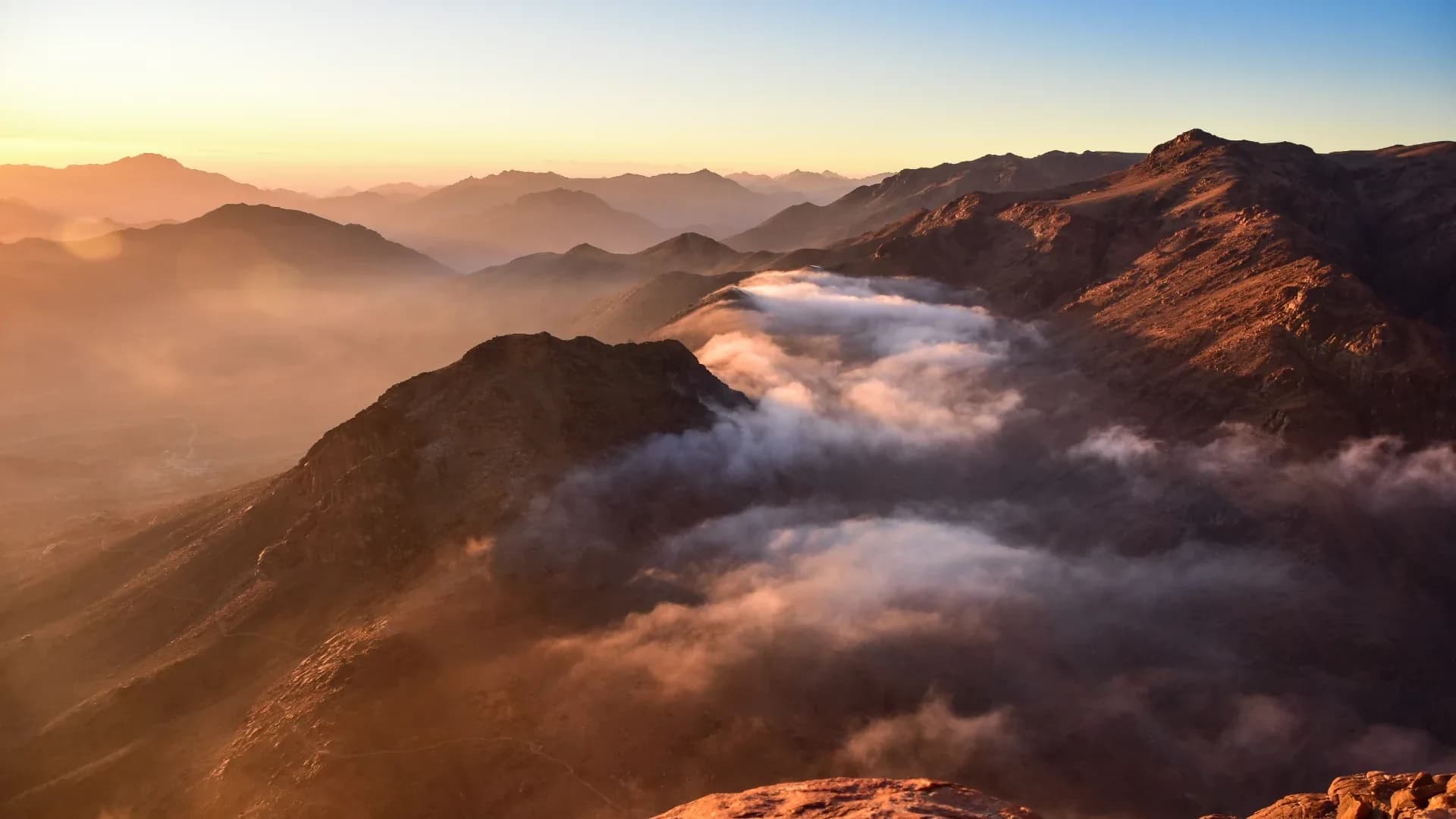 Sunrise over the Sinai mountains from the summit of Mount Sinai, with clouds in the valleys